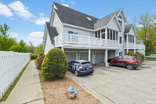 view of side of home with fence, a shingled roof, an attached garage, aphalt driveway, and a sunroom