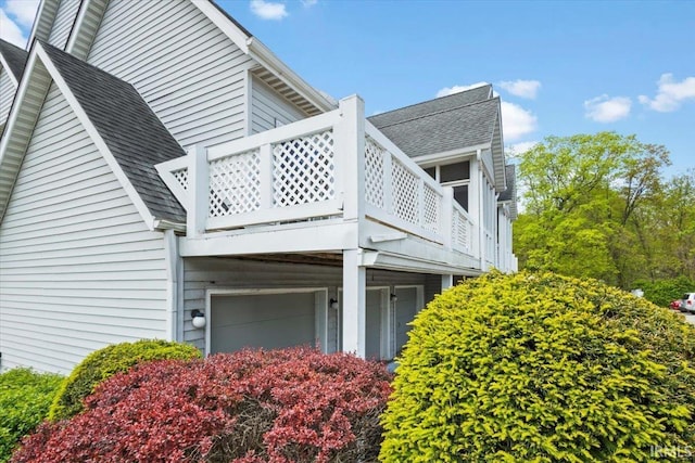 view of side of home with a shingled roof, an attached garage, and a balcony