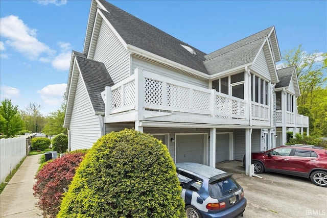 view of property exterior with a shingled roof, an attached garage, a sunroom, a balcony, and driveway