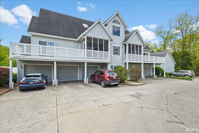 view of property featuring a sunroom, a garage, roof with shingles, and driveway