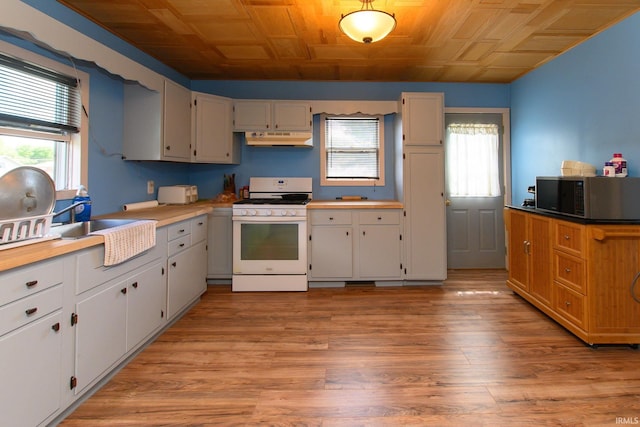 kitchen with light wood-style floors, light countertops, stainless steel microwave, under cabinet range hood, and white range with gas cooktop