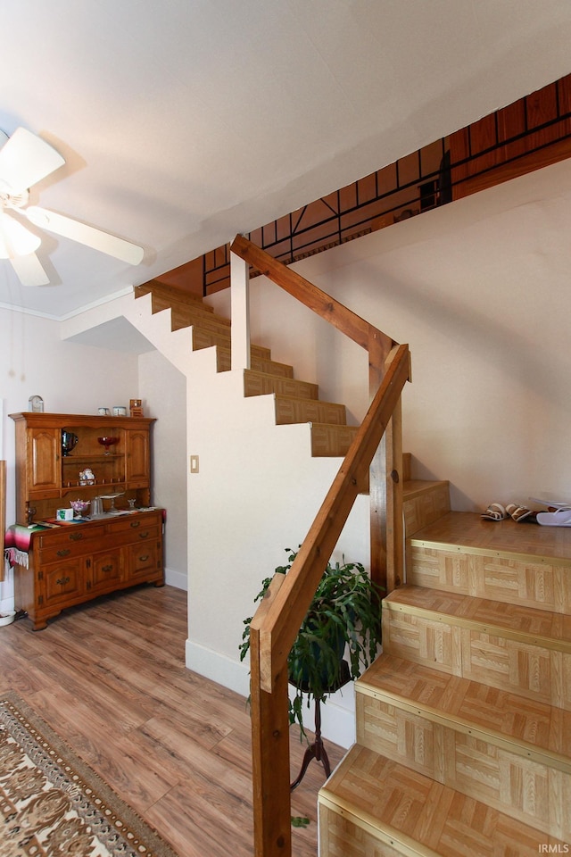 staircase featuring baseboards, a ceiling fan, and wood finished floors