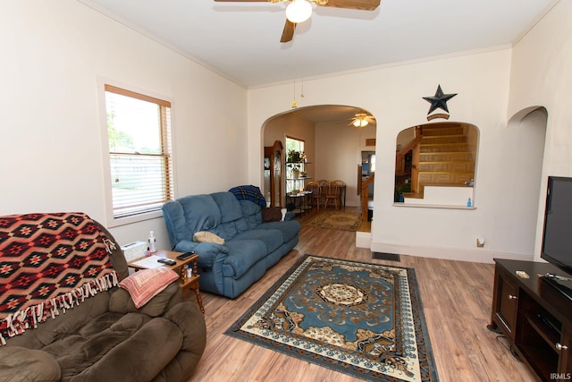 living area with ornamental molding, arched walkways, a ceiling fan, and light wood-type flooring
