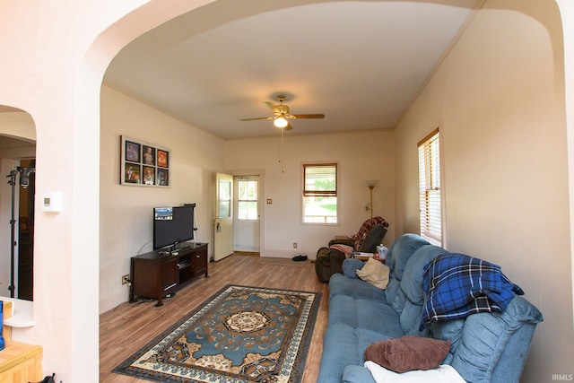 living area with arched walkways, a ceiling fan, wood finished floors, and baseboards