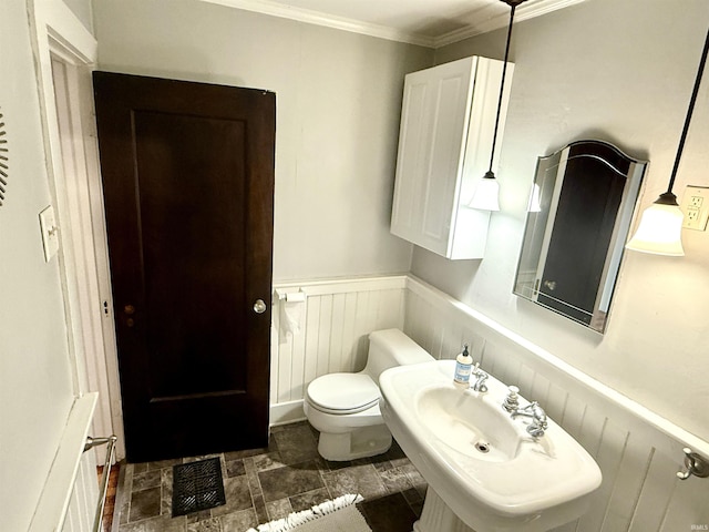 half bathroom with wainscoting, stone finish floor, toilet, visible vents, and crown molding