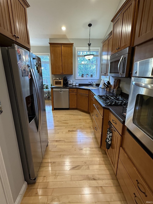 3201 E Kristen Ct, Bloomington, IN 47401 - kitchen with stainless steel appliances, light wood-style flooring, dark countertops, brown cabinetry, and hanging light fixtures