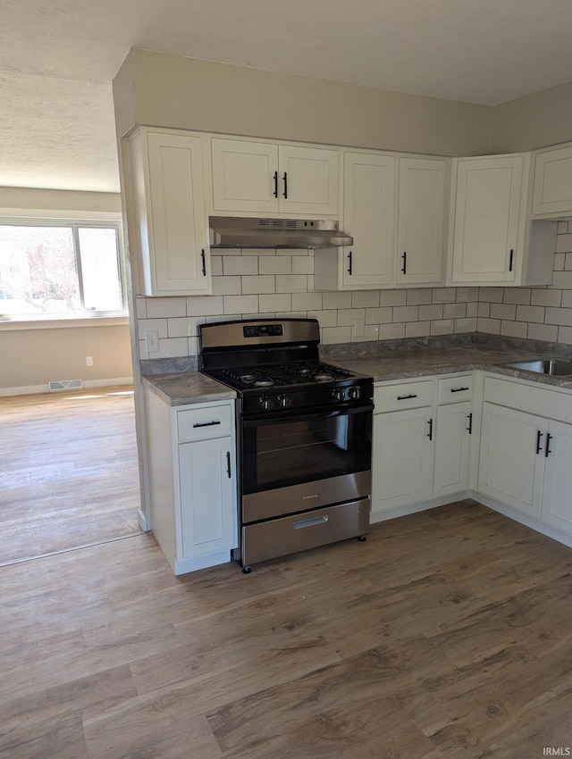 kitchen featuring white cabinets, stainless steel range with gas cooktop, visible vents, decorative backsplash, and under cabinet range hood