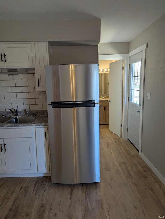 kitchen featuring a sink, decorative backsplash, light wood finished floors, white cabinets, and freestanding refrigerator