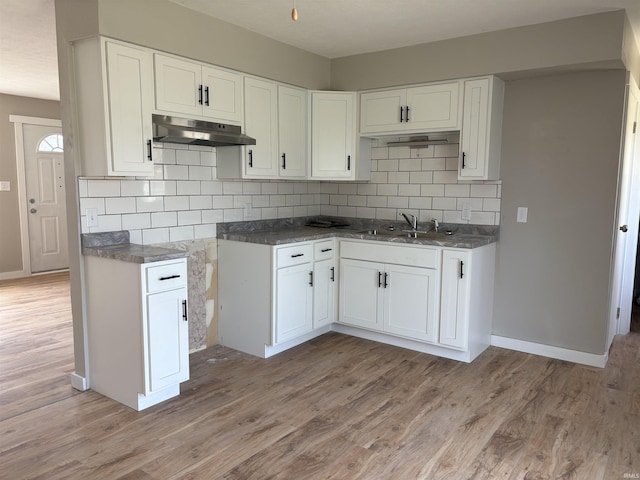 kitchen with a sink, decorative backsplash, light wood-type flooring, white cabinetry, and under cabinet range hood