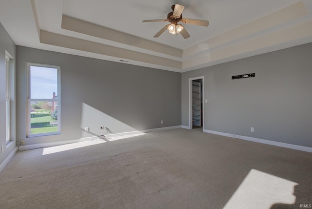 unfurnished room with ceiling fan, light carpet, a tray ceiling, and baseboards