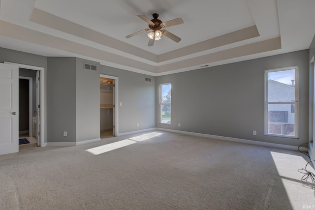 unfurnished bedroom with a walk in closet, baseboards, a tray ceiling, and light colored carpet
