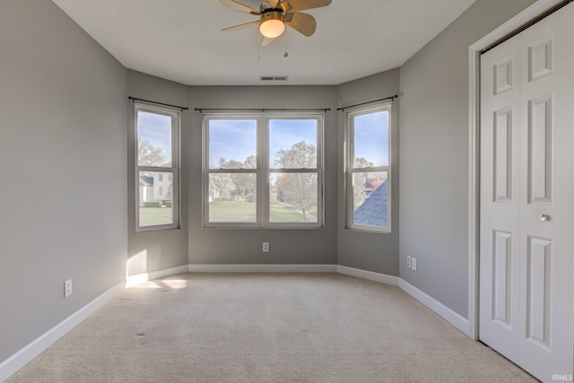 carpeted spare room featuring plenty of natural light, visible vents, a ceiling fan, and baseboards