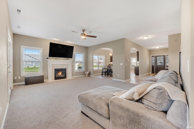 living area featuring light carpet, arched walkways, baseboards, visible vents, and a ceiling fan