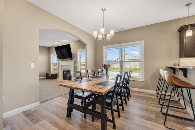 dining space with light wood-type flooring, arched walkways, a fireplace, baseboards, and visible vents