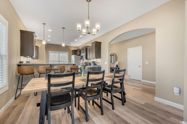 dining space featuring a chandelier, arched walkways, light wood-style flooring, baseboards, and recessed lighting