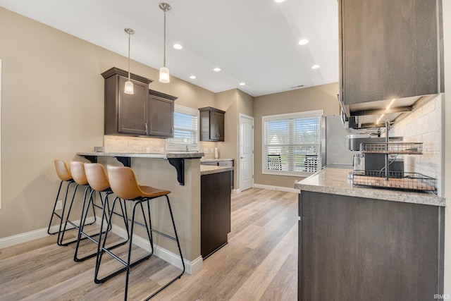 kitchen featuring a peninsula, light wood-style flooring, tasteful backsplash, baseboards, and a breakfast bar area