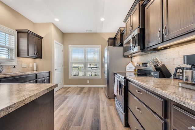 kitchen with stainless steel appliances, light wood-style flooring, baseboards, dark brown cabinetry, and decorative backsplash