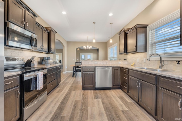 kitchen with a sink, dark brown cabinets, backsplash, a chandelier, and appliances with stainless steel finishes