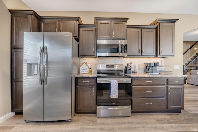 kitchen featuring decorative backsplash, appliances with stainless steel finishes, dark brown cabinets, and light wood-style flooring