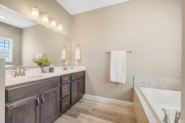 full bath with a garden tub, wood finished floors, a sink, and double vanity