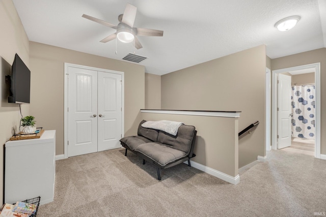 living area with a ceiling fan, visible vents, an upstairs landing, and carpet flooring