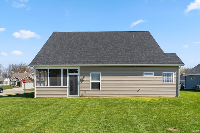 rear view of house with roof with shingles, a sunroom, and a yard