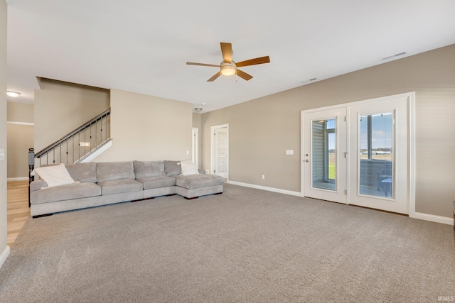 unfurnished living room featuring a ceiling fan, baseboards, carpet, and stairs