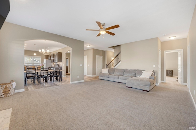 living room featuring arched walkways, baseboards, light colored carpet, and ceiling fan