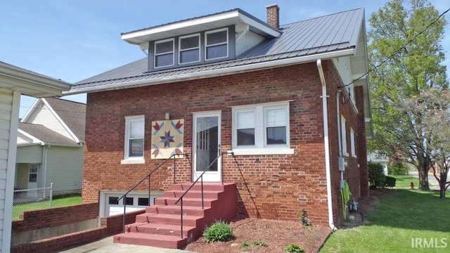 view of front of home with brick siding, a chimney, a front lawn, and metal roof