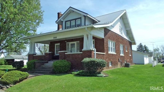 view of front of property featuring a chimney, a front lawn, cooling unit, covered porch, and brick siding