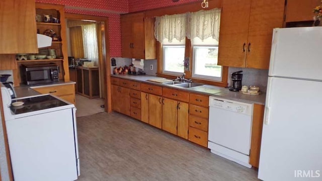 kitchen with a sink, wallpapered walls, brown cabinetry, white appliances, and light countertops