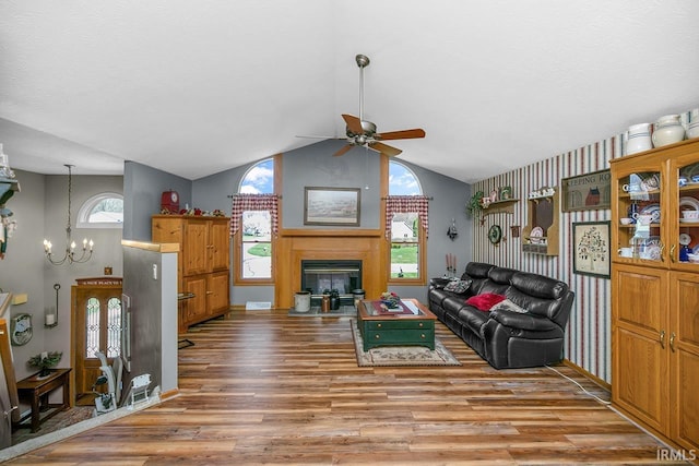living area with a fireplace with flush hearth, lofted ceiling, wood finished floors, and ceiling fan with notable chandelier