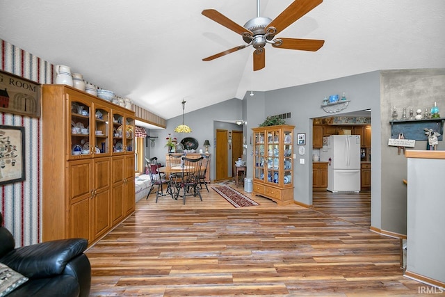 living room featuring baseboards, vaulted ceiling, a ceiling fan, and light wood-type flooring
