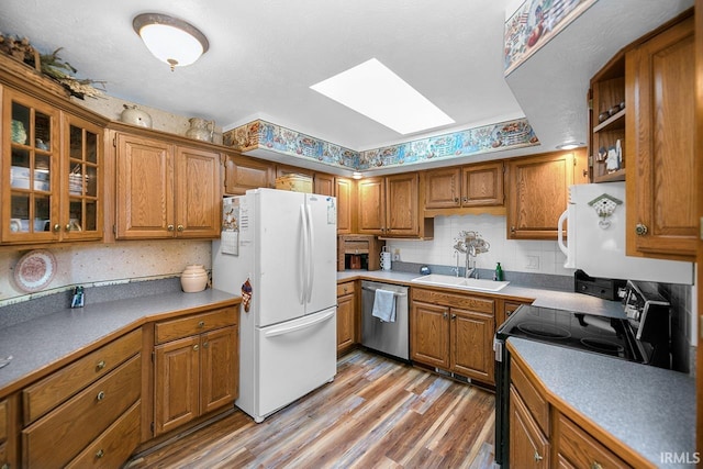 kitchen featuring a skylight, brown cabinetry, dishwasher, electric range, and freestanding refrigerator