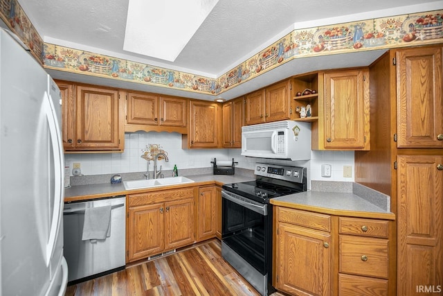kitchen with stainless steel appliances, a sink, wood finished floors, brown cabinets, and open shelves