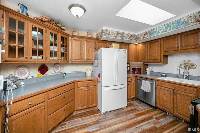 kitchen with a sink, a skylight, brown cabinetry, dishwasher, and freestanding refrigerator