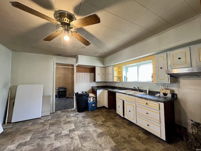 kitchen featuring a ceiling fan, dark countertops, a sink, and stone finish flooring