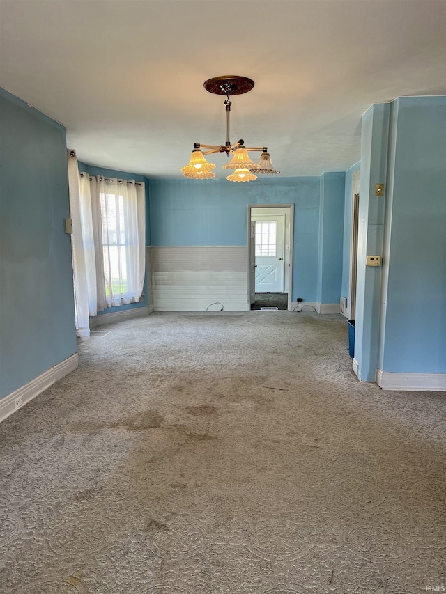 empty room featuring carpet floors, baseboards, and a notable chandelier