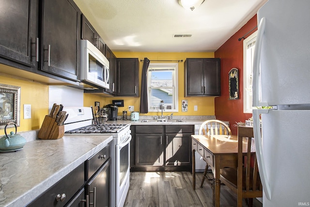 kitchen featuring light countertops, visible vents, a sink, white appliances, and dark wood-style flooring