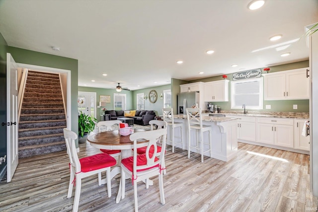 dining room with recessed lighting, light wood-type flooring, a healthy amount of sunlight, and stairs