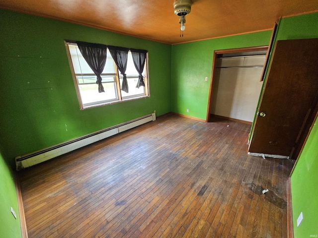 unfurnished bedroom featuring a baseboard heating unit, baseboards, a closet, and hardwood / wood-style flooring