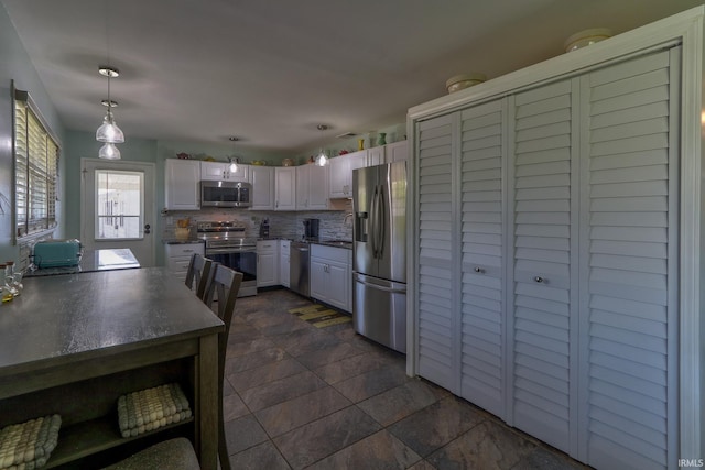 kitchen with white cabinets, a sink, dark countertops, backsplash, and appliances with stainless steel finishes