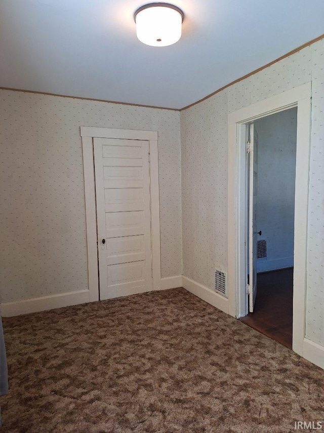 carpeted empty room featuring wallpapered walls, visible vents, and ornamental molding