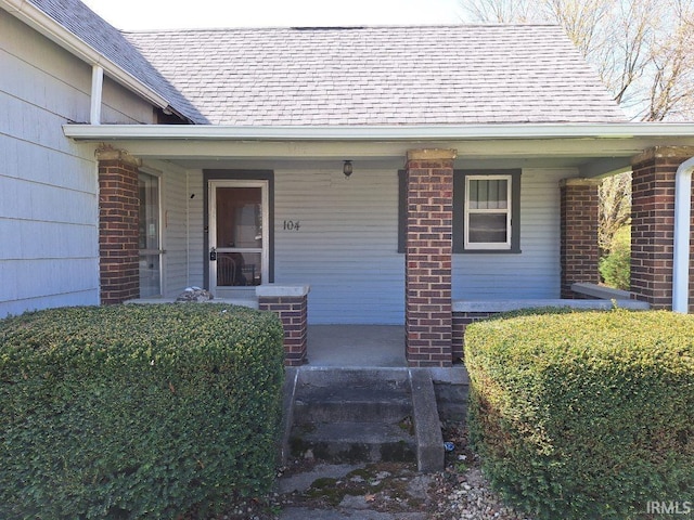 property entrance featuring brick siding, a porch, and a shingled roof
