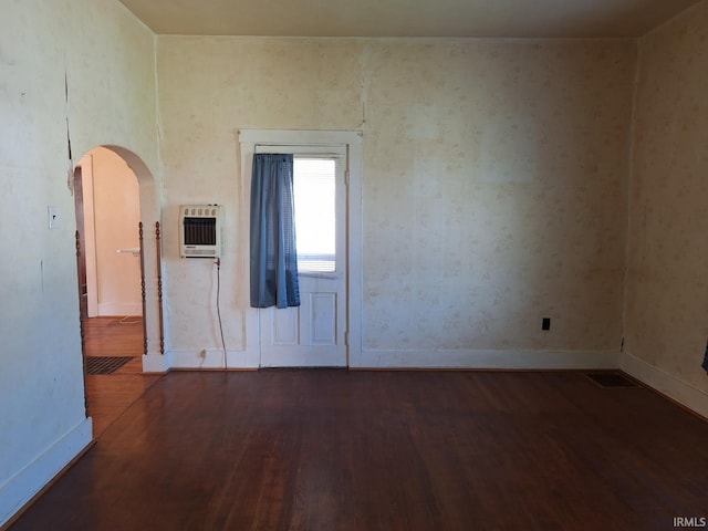 spare room with arched walkways, wood finished floors, baseboards, and heating unit