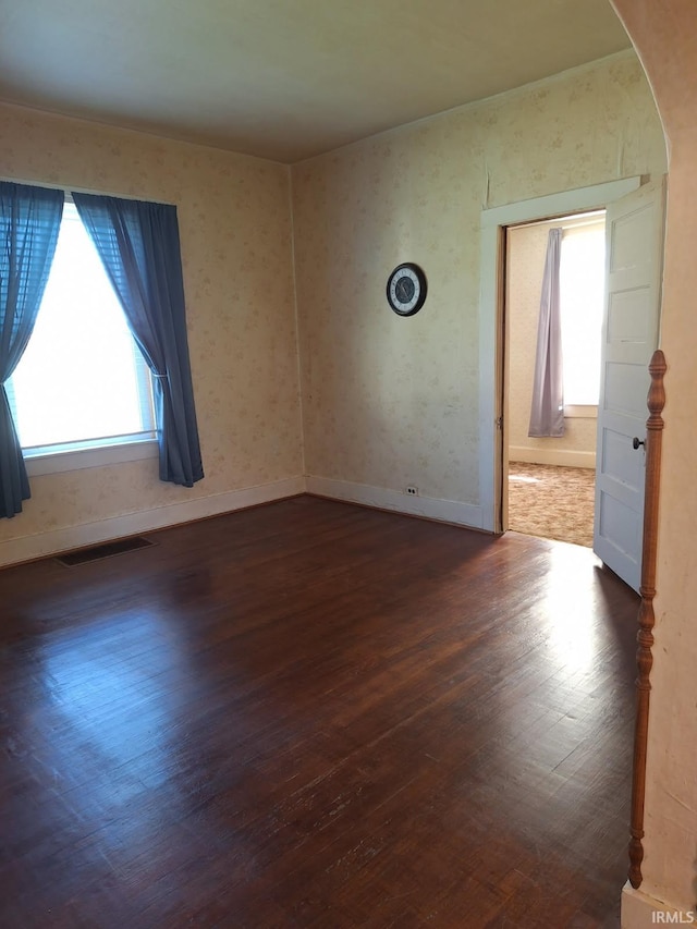 spare room with arched walkways, dark wood finished floors, visible vents, and baseboards
