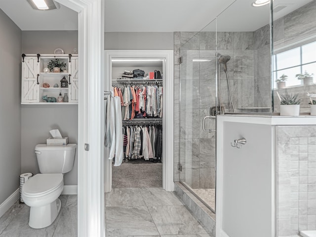 bathroom featuring a shower stall, marble finish floor, toilet, a walk in closet, and baseboards