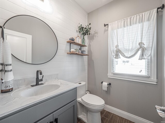 bathroom featuring toilet, baseboards, wood walls, wood finished floors, and vanity