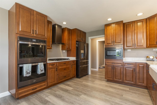 kitchen featuring multiple ovens, built in microwave, gas cooktop, stainless steel fridge, and wall chimney exhaust hood