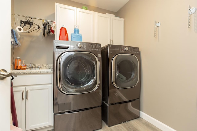 clothes washing area with washing machine and dryer, baseboards, light wood finished floors, and cabinet space